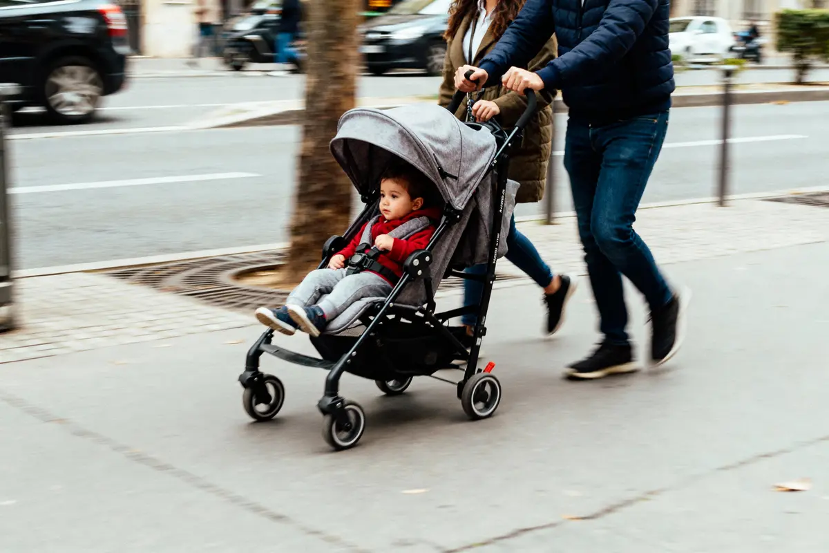 Un enfant dans une poussette est poussé par deux adultes marchant sur un trottoir urbain.