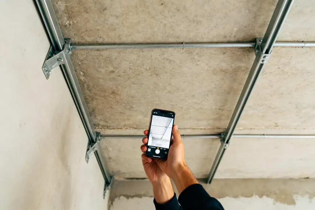Un plafond avec structures métalliques photographié par une main tenant un smartphone vers le haut.