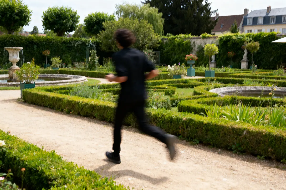Homme courant dans un jardin bien entretenu avec buissons taillés et fontaines. Arrière-plan verdoyant.
