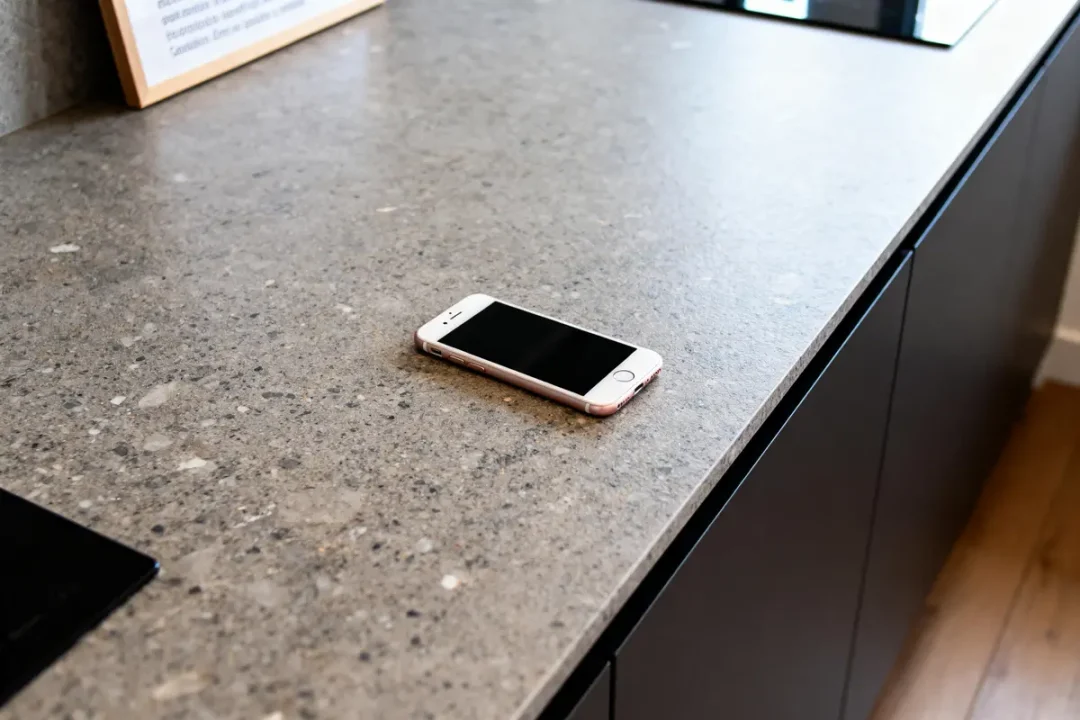 Un smartphone rose posé sur un plan de travail en granit gris dans une cuisine moderne.