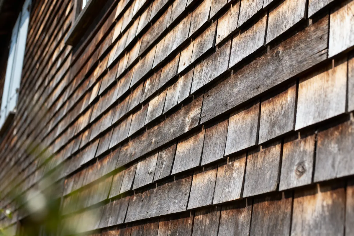 Façade en bois avec bardeaux, éclairée par le soleil, en perspective diagonale.