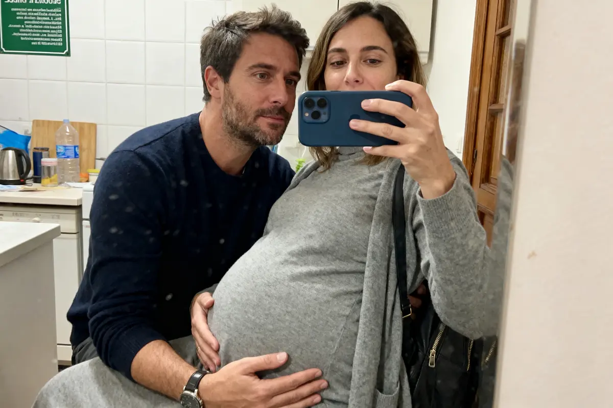 Un couple prend un selfie dans la cuisine, l'homme touche le ventre enceinte de la femme.