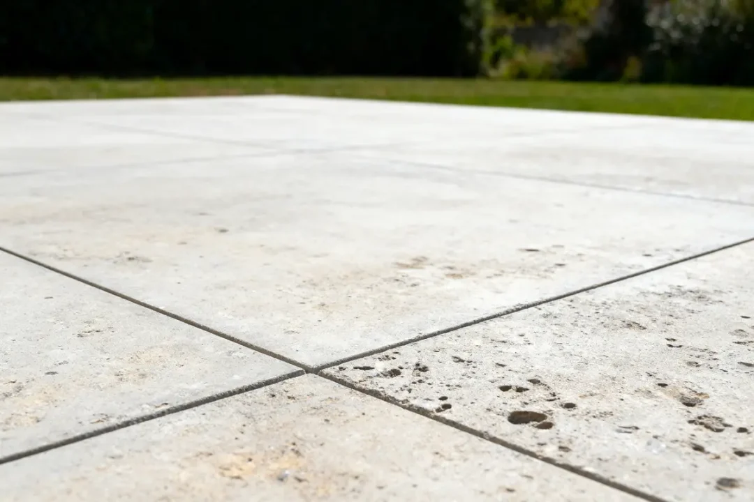 Dalles en béton texturé avec joints, jardin en arrière-plan flou, soleil lumineux.
