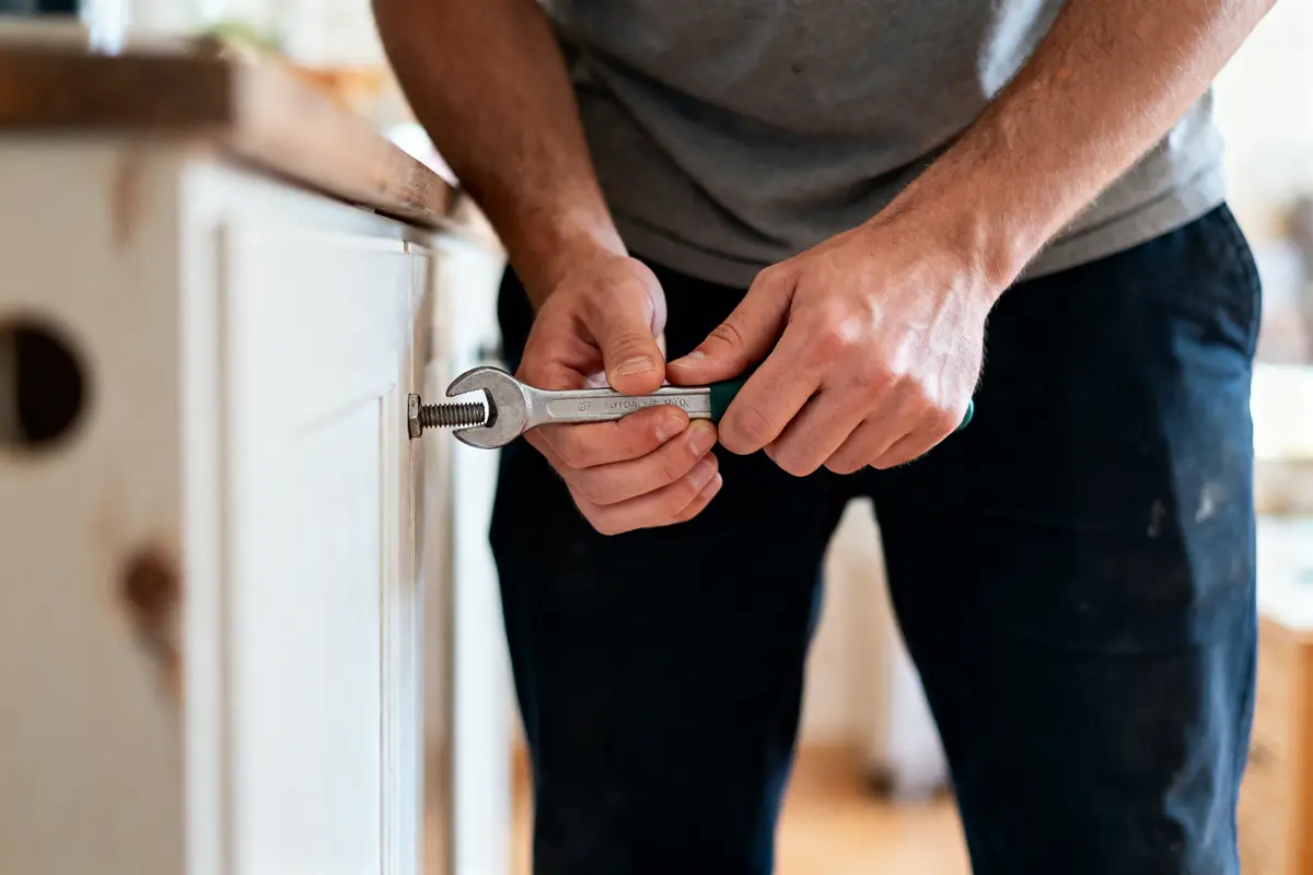 Personne utilisant une clé pour serrer un boulon sur un meuble en bois clair.