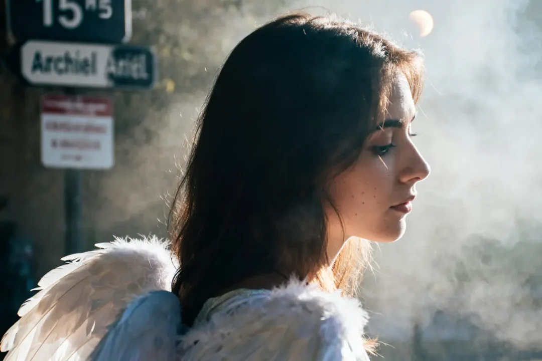 Femme profil, ailes d'ange blanches, soleil, brume, panneaux signalisation en arrière-plan flou.