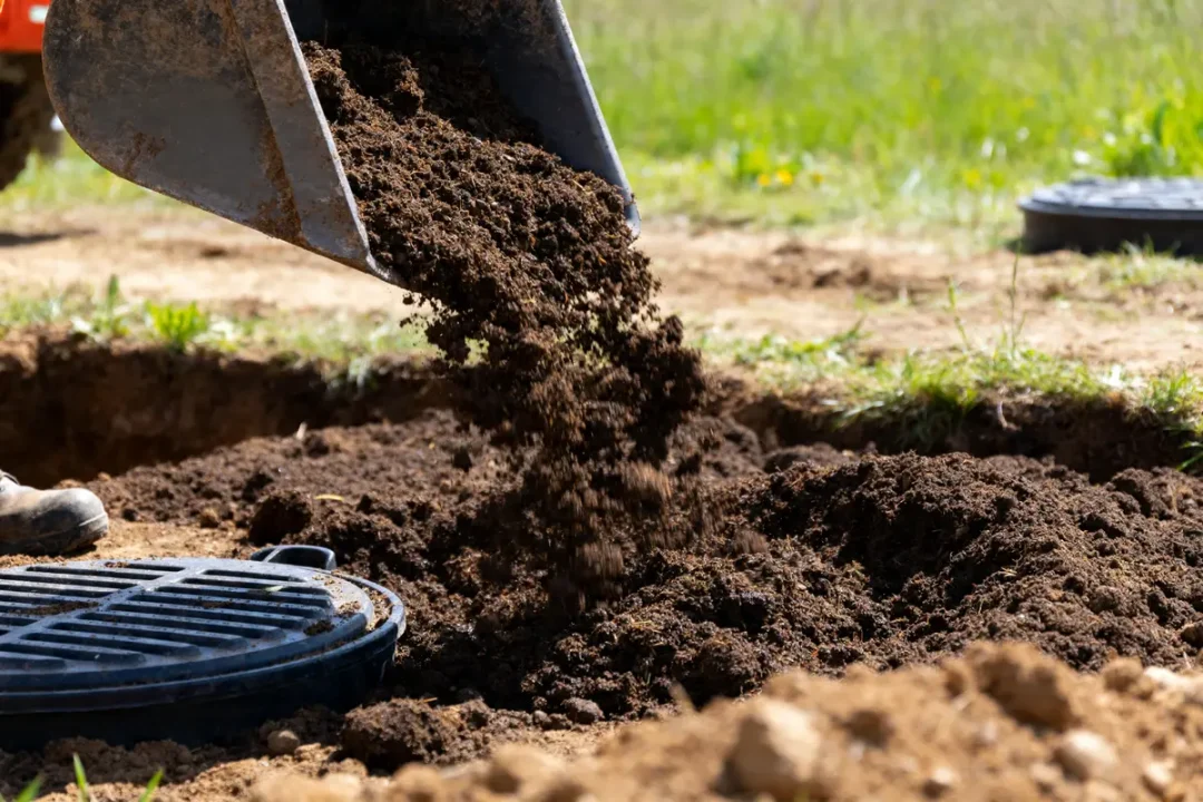 Terre déversée autour de l'ouverture pour l'épandage fosse septique dans un jardin.