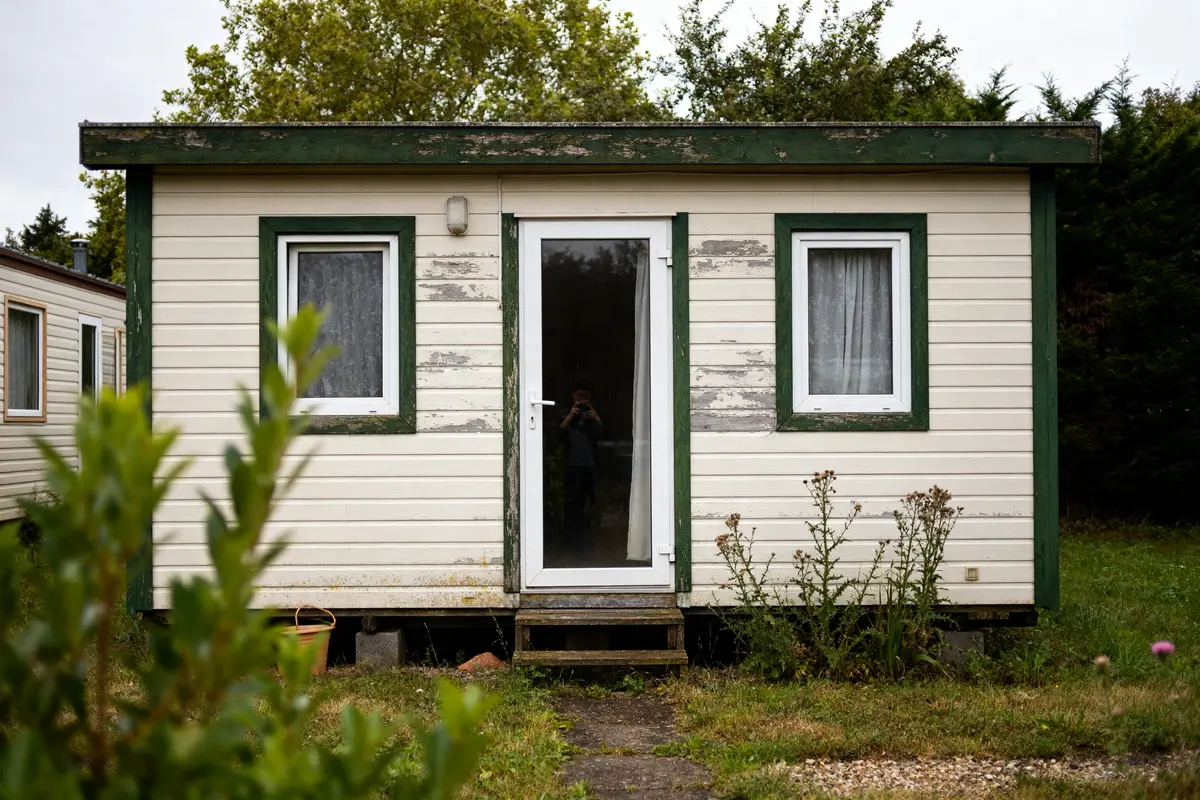 Façade avant d'une petite maison en préfabriqué entourée de végétation luxuriante
