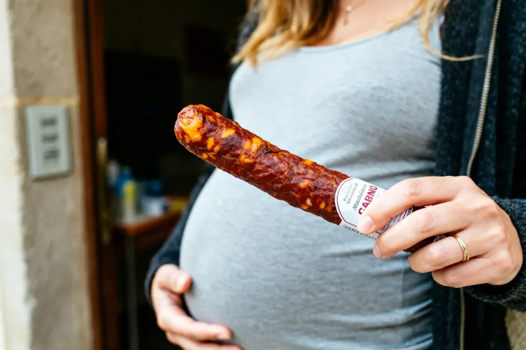 Femme enceinte tenant un cervelas devant son ventre arrondi en arrière-plan flou