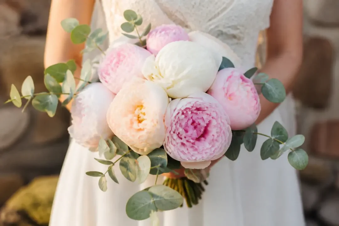 Mariée tenant un bouquet de pivoines roses et blanches avec feuillage vert élégant