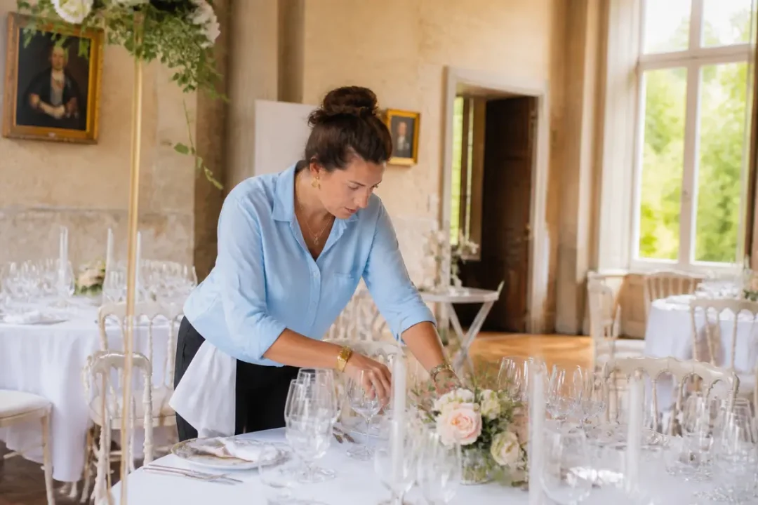 Décoratrice événementielle préparant une table élégante avec fleurs et verres pour une réception